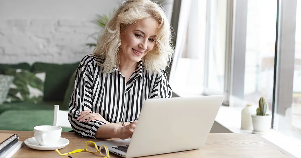 Stylish blonde mature-aged female worker on her laptop at home wearing striped blouse. Blog title: Breaking age barriers: Why we must rethink work, age, and progress